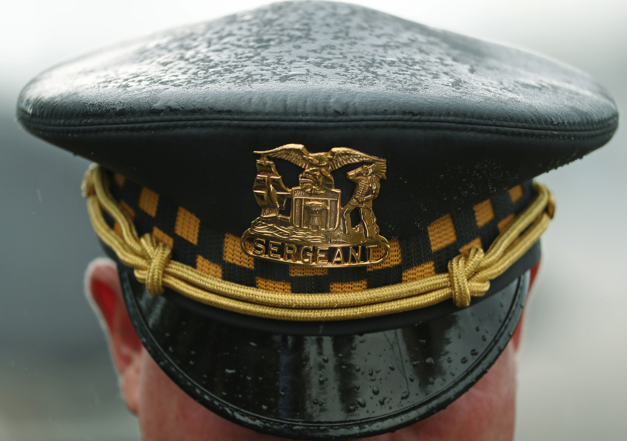 Rain falls on a police sergeant's crown cap outside the...
