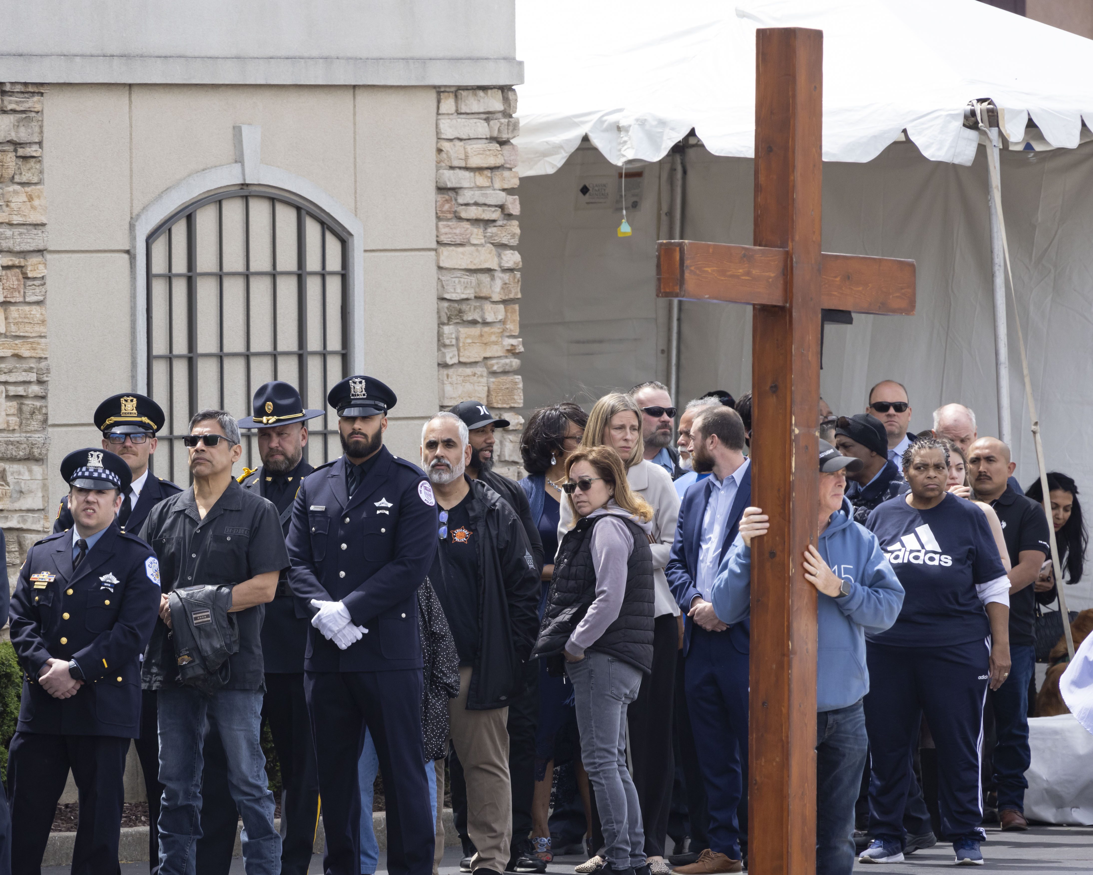 A man holds a large cross while police officers and members of the public line up to enter the visitation for Chicago police Officer Luis M. Huesca on April 28, 2024, at Blake-Lamb Funeral Home in Oak Lawn. Huesca, a CPD officer for six years, was returning home last week after a shift in the Calumet District when he was fatally shot. (Brian Cassella/Chicago Tribune)