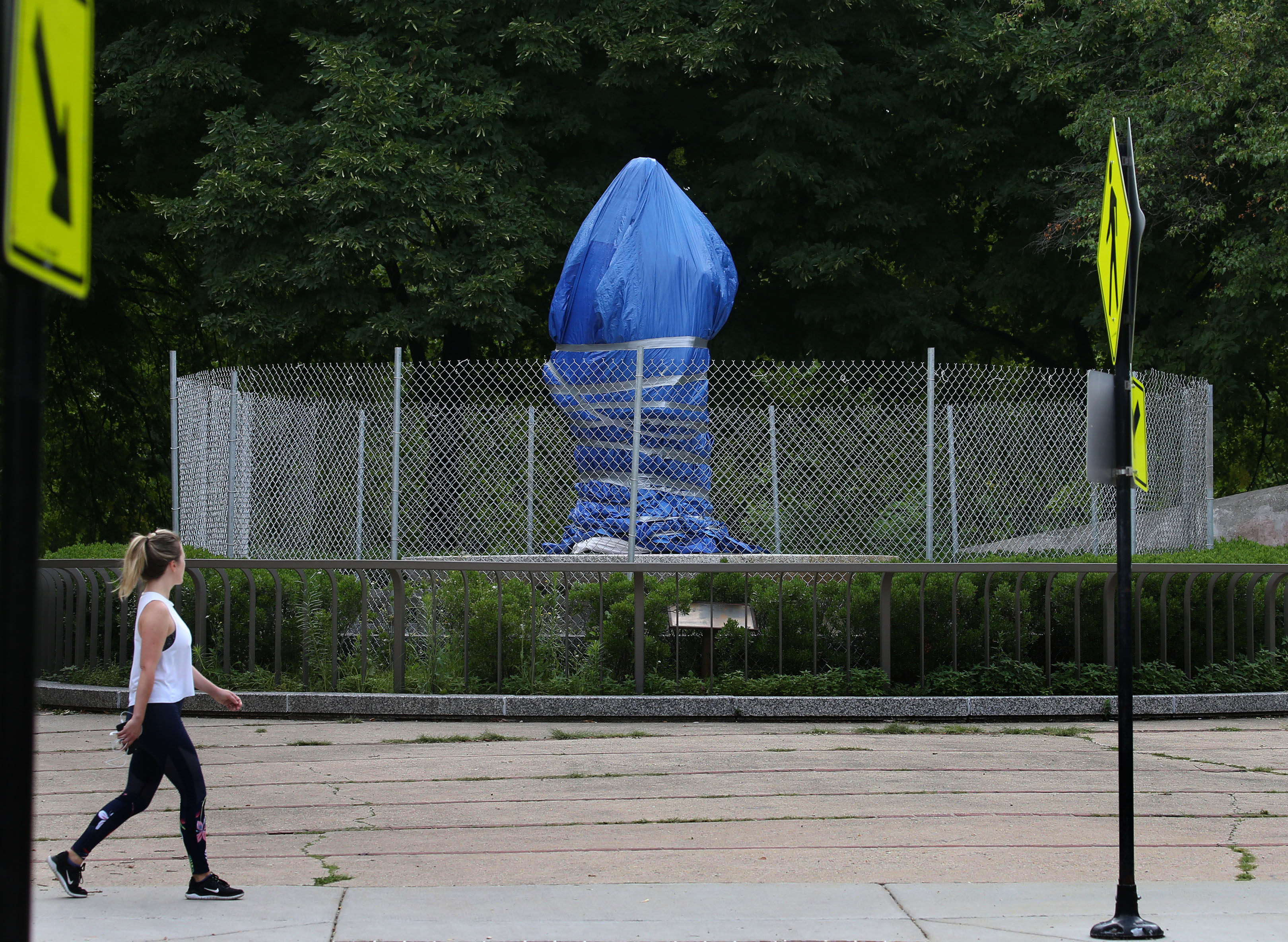 A person passes a tarp-covered Christopher Columbus statue at Arrigo Park on July 21, 2020. (Antonio Perez/Chicago Tribune)